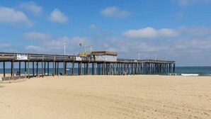 A beach with a wooden pier extending into the ocean, a small building at the end, and a clear sky. - Makai 403 (Ocean City)