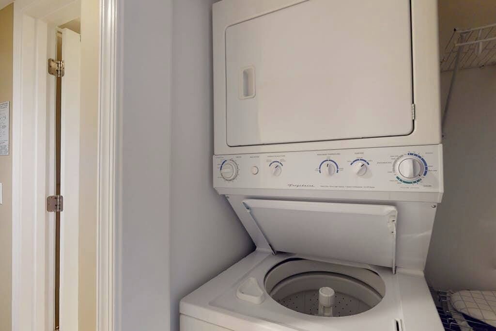 A front-loading washing machine with a control panel, a door, and a wall-mounted drying rack.