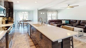 Une cuisine moderne dotée d’un îlot central, d’un coin repas et d’un salon avec un canapé et un ventilateur de plafond.