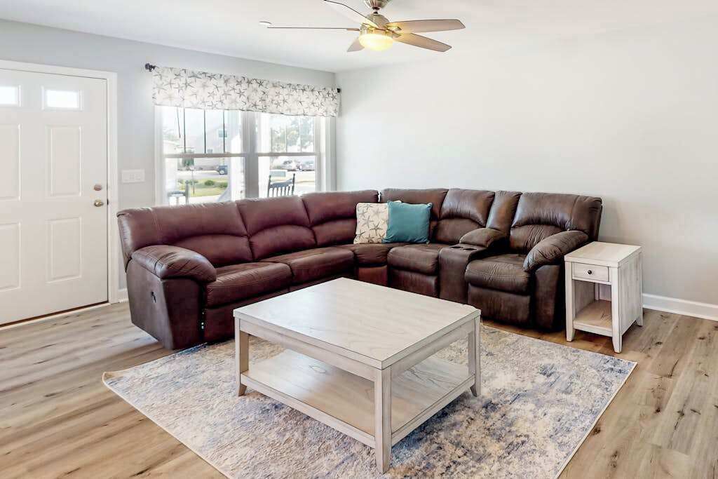 A living room with a sectional sofa, a coffee table, a side table, and a ceiling fan.