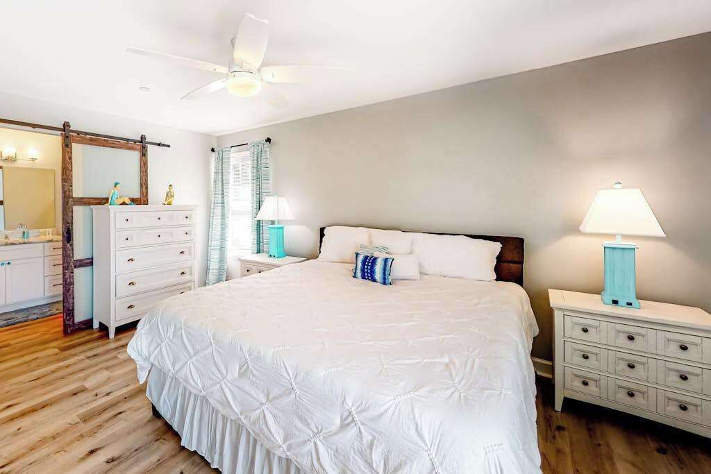 Un dormitorio con cama, cómoda, mesita de noche, lámpara, ventilador de techo y espejo.
