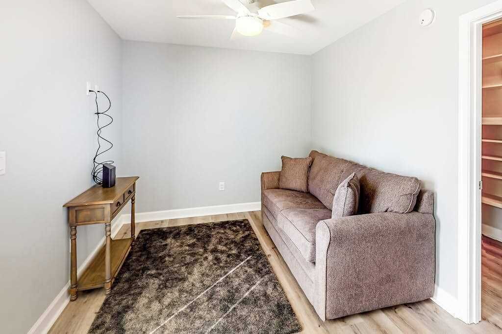 A room with a ceiling fan, a brown sofa, a wooden side table, and a patterned rug.