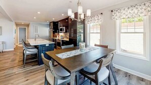 Une cuisine moderne avec des meubles de couleur sombre, un îlot central et un coin repas comprenant une table et des chaises en bois.