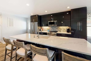 A modern kitchen with dark cabinets, a large island, and a built-in oven. - New home steps from Northside Park with shared pools, tennis & pickleball (Ocean City)