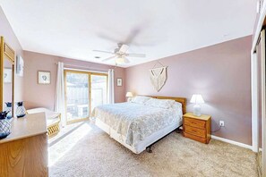 Ein Schlafzimmer mit Bett, Nachttischen, Deckenventilator und Blick durch eine Glastür.