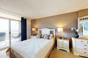 A hotel room with a bed, two bedside tables with lamps, a dresser, and a balcony with chairs. - Fountainhead Towers 310 (Ocean City)