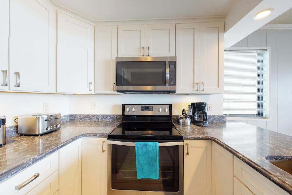 A kitchen with white cabinets, a stainless steel microwave, a black stove, a toaster, and a kettle.