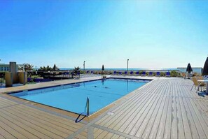 Un área de piscina con cubierta de madera, sillas de descanso y vista al mar.