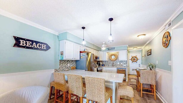 Una cocina con una isla central, armarios blancos, sillas de mimbre y un cartel que dice 'BEACH'.