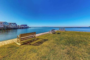 A waterfront property with a grassy area, wooden benches, and a dock extending into the water. - Bayspot A-101 (Ocean City)