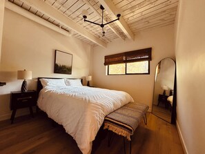 Un dormitorio con una cama, mesitas de noche, un banco, una ventana, un ventilador de techo y un espejo.