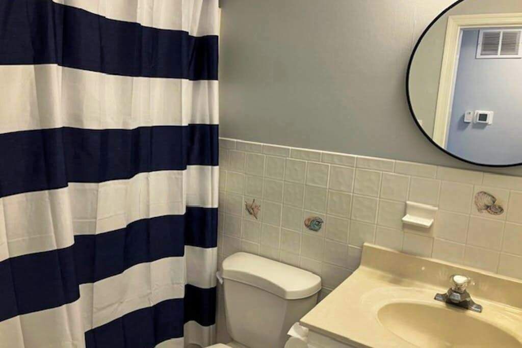 Un baño con cortina de ducha a rayas, un inodoro, un lavabo y un espejo.