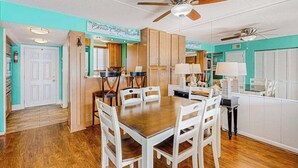 A dining area with a wooden table and white chairs, a ceiling fan, and a kitchen area with cabinets and a countertop. - Wight Bay North 439 (Ocean City)