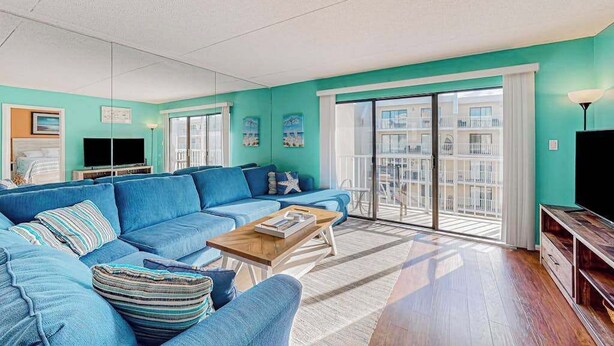 A living room with a blue sofa, a wooden coffee table, and a large window with a view of a building. - Wight Bay North 439 (Ocean City)