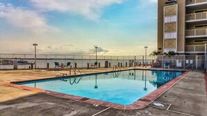 A swimming pool with a metal fence, a building with balconies, and a clear sky. - Wight Bay North 439 (Ocean City)