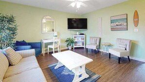 Un salon avec un canapé, une table basse, un téléviseur et un ventilateur de plafond.
