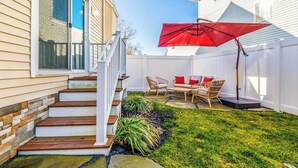 Un jardin avec un escalier en bois, un parasol rouge et du mobilier d’extérieur.