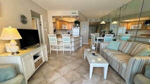 Un salon comprenant un téléviseur, un canapé, une table basse, ainsi qu’un coin cuisine avec une table à manger et des chaises.
