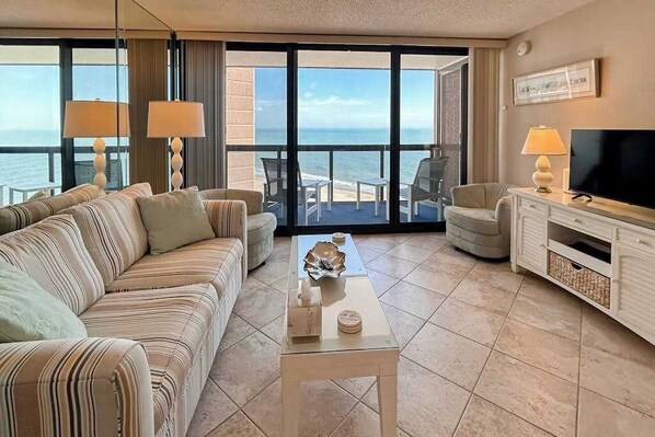 A hotel room with a large balcony, a sofa, a TV, and a coffee table. - Spacious oceanfront condo with indoor pool, sauna, game room, great beach access (Ocean City)