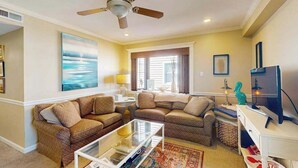 A living room with two sofas, a coffee table, a ceiling fan, a television, and a painting on the wall.