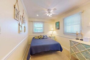 A bedroom with a bed, ceiling fan, two windows with blinds, a bedside table with a lamp, and wall-mounted picture frames. - Sunny condo w/balconies, full kitchen, A/C & Wifi & just steps to the beach (Ocean City)