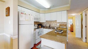 A kitchen with white cabinets, a granite countertop, a microwave, and a stove.