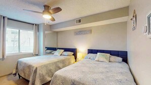 Een slaapkamer met twee bedden, een plafondventilator en een raam met jaloezieën.