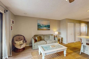 A living room with a sofa, a rocking chair, a coffee table, a painting, and a lamp. - Jamaica Bay 202B (Ocean City)