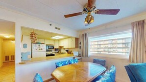 A dining area with a wooden table and blue upholstered chairs, a ceiling fan, and a view of the outside through a window. - Excalibur 107 (Ocean City)
