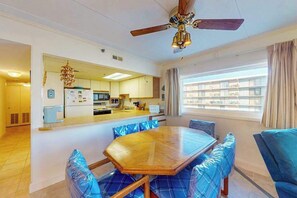 Un comedor con una mesa de madera y sillas tapizadas en azul, un ventilador de techo y vistas al exterior a través de un ventanal.