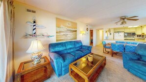A living room with a blue sofa, a coffee table, a lamp, and a painting of a lighthouse. - Excalibur 107 (Ocean City)