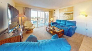 A living room with a sofa, armchair, and coffee table, a television, and a painting on the wall. - Excalibur 107 (Ocean City)