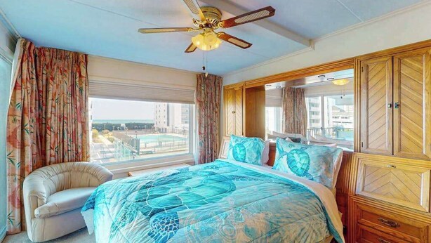 A bedroom with a bed, a chair, a ceiling fan, and a view of the city. - Excalibur 107 (Ocean City)