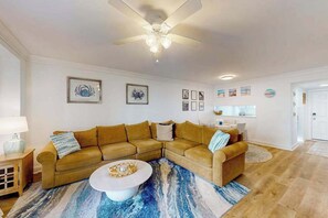 Ein Wohnzimmer mit Ecksofa, Couchtisch, Deckenventilator und Wandbildern.