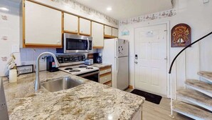 Cozinha com bancada de granito, eletrodomésticos de aço inoxidável e porta branca com um prato decorativo.