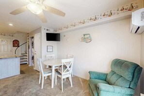 Ein Zimmer mit Esstisch, Stühlen, Deckenventilator, Fernseher und einem grünen Sofa.
