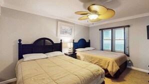 Une chambre avec deux lits, un ventilateur de plafond, une fenêtre avec des stores et un tableau encadré au mur.