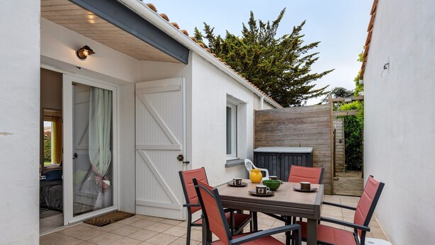 A patio with a table and chairs, a wooden fence, and a door leading to a covered area.