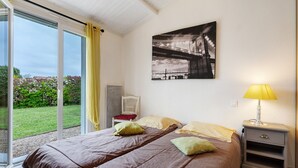 A bedroom with a bed, a nightstand, a lamp, a chair, and a large window with curtains.