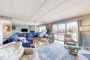 Ein modernes Wohnzimmer mit Ecksofa, Couchtisch, Liegesessel und großem Fenster mit Blick auf die Stadt.