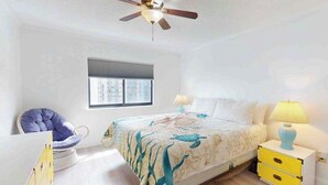 A bedroom with a bed, a chair, a nightstand, a lamp, a ceiling fan, and a window. - Camelot 603B (Ocean City)