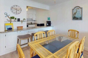 A modern kitchen with white cabinets, a dining table with chairs, a clock, and a coffee machine. - Luxury Ocean View Condo w/Shared Olympic Pool, Tennis, balcony & WiFi (Ocean City)
