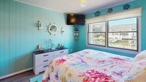 A bedroom with a bed, a dresser, a ceiling fan, a TV, and a window with a view of a dock and boats. - Sunny canal side condo - w/balcony, short walk to the beach, boardwalk, & parks (Ocean City)