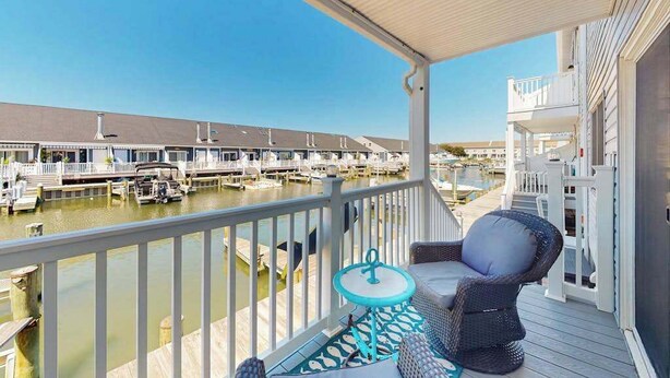 A balcony with a view of a marina, a wicker chair, and a small table. - Sunny canal side condo - w/balcony, short walk to the beach, boardwalk, & parks (Ocean City)