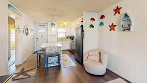 A kitchen with a refrigerator, a dining table, and chairs. There is a starfish decoration on the wall and a starfish rug on the floor. - Sunny canal side condo - w/balcony, short walk to the beach, boardwalk, & parks (Ocean City)