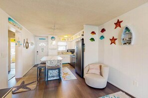 A kitchen with a refrigerator, a dining table, and chairs. There is a starfish decoration on the wall and a starfish rug on the floor. - Sunny canal side condo - w/balcony, short walk to the beach, boardwalk, & parks (Ocean City)