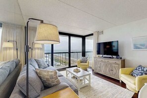 A modern living room with a sofa, armchair, coffee table, and TV. - Charming Beach Condo w/Balcony, beach & bay views, Pools, Gym, Tennis, W/D & A/C (Ocean City)