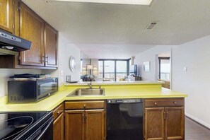 A kitchen with wooden cabinets, a microwave, a dishwasher, and a yellow countertop. - Charming Beach Condo w/Balcony, beach & bay views, Pools, Gym, Tennis, W/D & A/C (Ocean City)