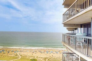 Un hôtel en bord de mer doté de balcons donnant sur l’océan, une plage de sable avec des parasols et un ciel dégagé.
