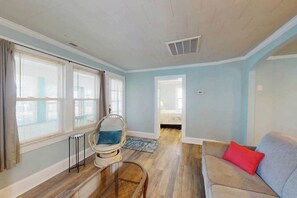 A room with a wooden floor, a grey sofa, a wicker chair, and a window with blinds. - Cute Ocean City single family home with Central AC & W/D (Ocean City)